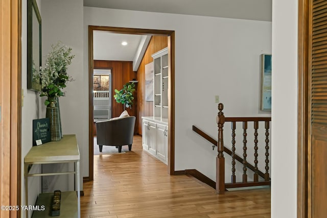 hall with light wood-type flooring, an upstairs landing, and baseboards