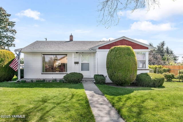 view of front of property with concrete block siding, a front lawn, a chimney, fence, and a shingled roof