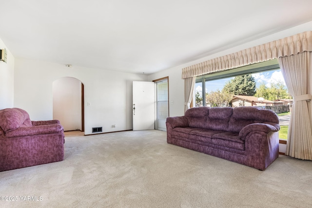living area featuring arched walkways, visible vents, and carpet flooring