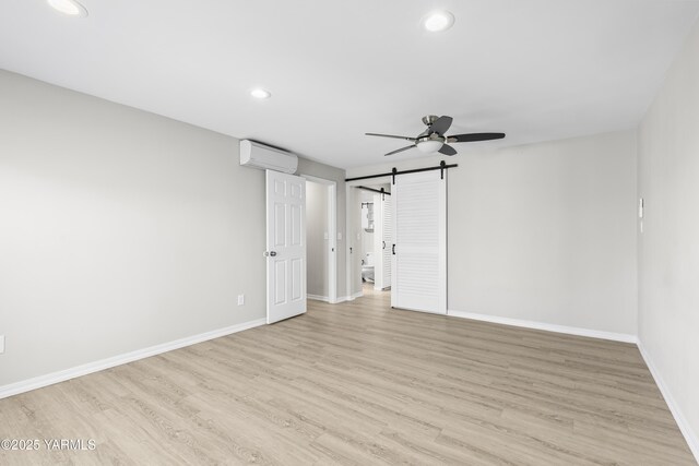 unfurnished room featuring a wall unit AC, recessed lighting, a barn door, light wood finished floors, and baseboards
