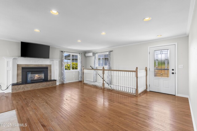 unfurnished living room featuring ornamental molding, hardwood / wood-style flooring, a wall mounted air conditioner, baseboards, and recessed lighting