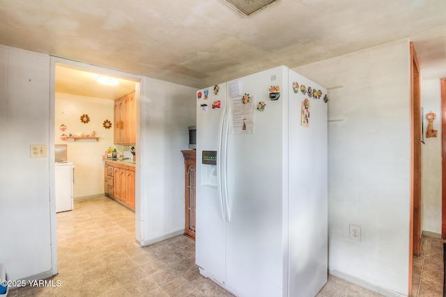 kitchen with white refrigerator with ice dispenser, baseboards, light countertops, light floors, and washer / clothes dryer