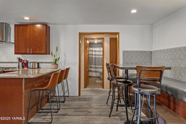 3603 Carol Ave, Yakima, WA 98902 - kitchen featuring a breakfast bar area, wall chimney exhaust hood, light stone countertops, wood finished floors, and tasteful backsplash
