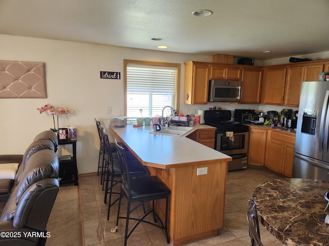 kitchen featuring stainless steel appliances, a sink, a kitchen bar, a peninsula, and recessed lighting