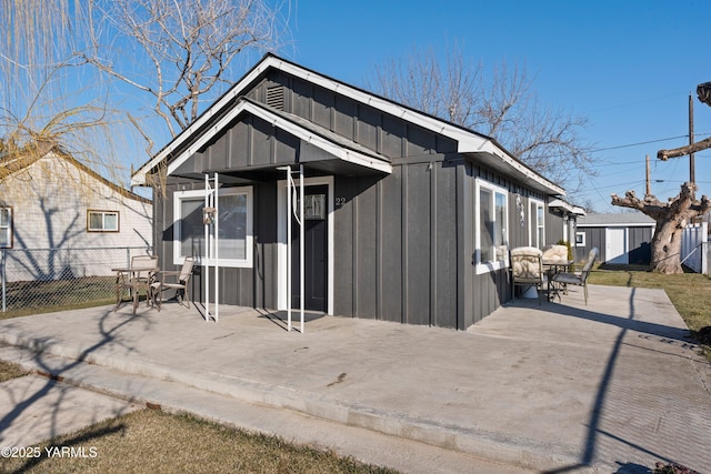 rear view of house featuring board and batten siding, a patio, and fence