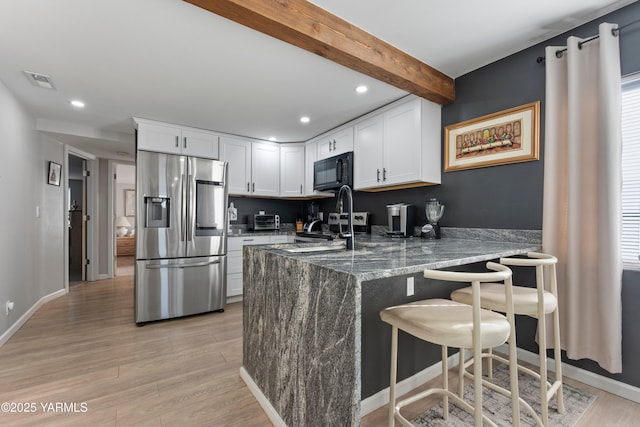 kitchen featuring visible vents, light wood-style floors, black microwave, stainless steel fridge, and beamed ceiling