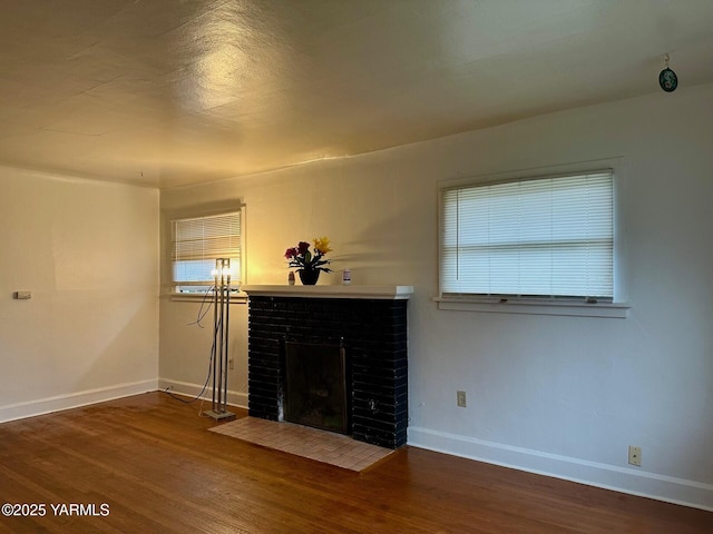 unfurnished living room featuring a brick fireplace, baseboards, and wood finished floors