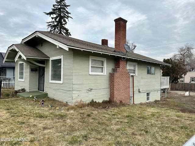 back of house with a chimney and a lawn