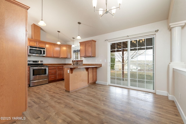 kitchen with light wood finished floors, a breakfast bar, a peninsula, appliances with stainless steel finishes, and a chandelier