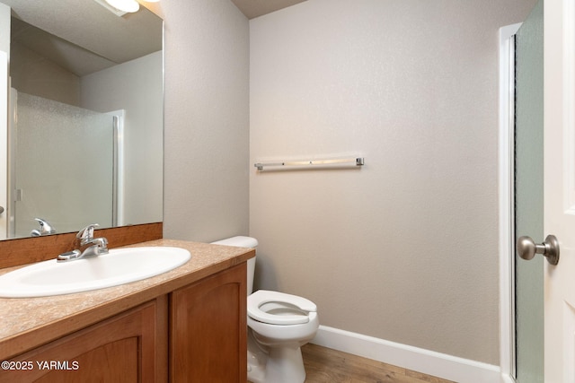 bathroom featuring toilet, wood finished floors, baseboards, walk in shower, and vanity