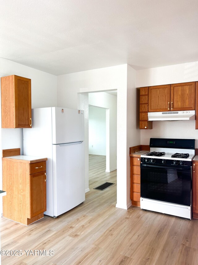 63 W Mead Ave, Yakima, WA 98902 - kitchen with range with gas cooktop, under cabinet range hood, freestanding refrigerator, light wood-style floors, and brown cabinets
