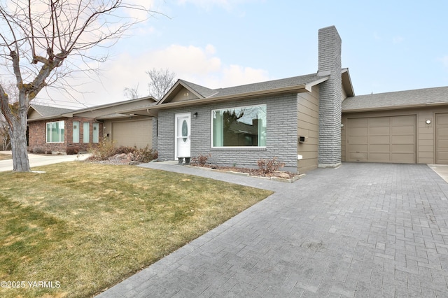 view of front of property with a garage, brick siding, decorative driveway, a chimney, and a front yard