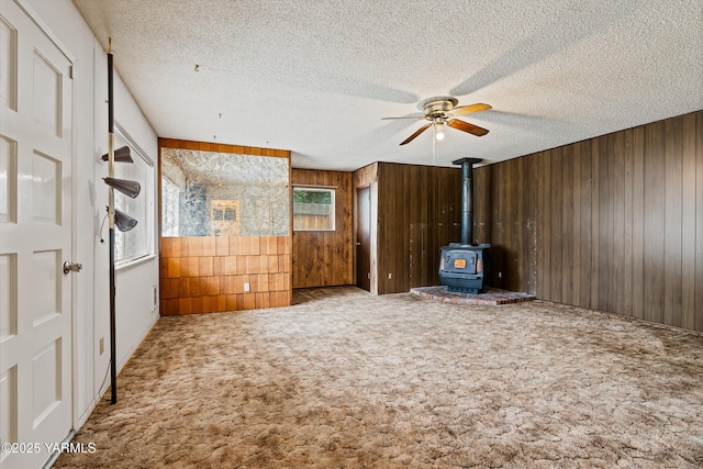 4905 Glenside Ct, Yakima, WA 98908 - carpeted empty room featuring wooden walls, ceiling fan, a wood stove, and a textured ceiling