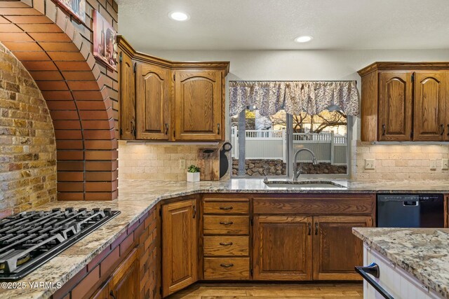 kitchen with a sink, tasteful backsplash, black appliances, and light stone counters