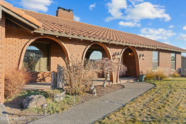 mediterranean / spanish house with a chimney, covered porch, a tile roof, and brick siding