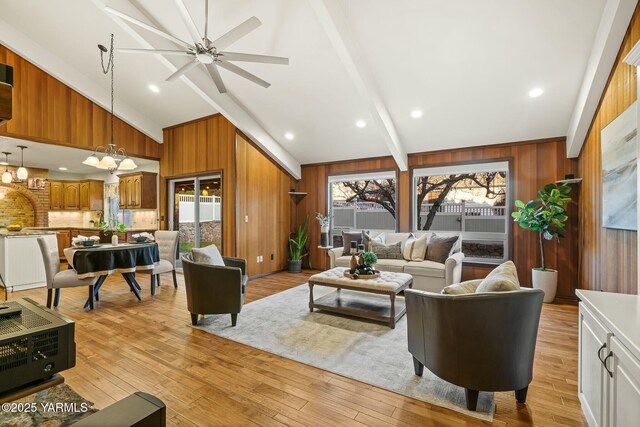 living area with wooden walls, beamed ceiling, ceiling fan, and light wood finished floors