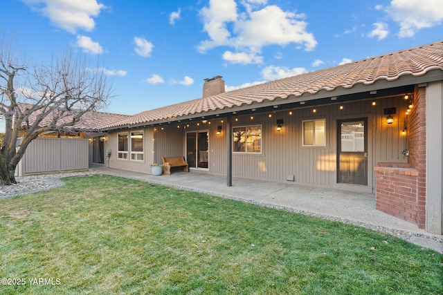 back of property featuring a patio, a chimney, a lawn, and a tiled roof