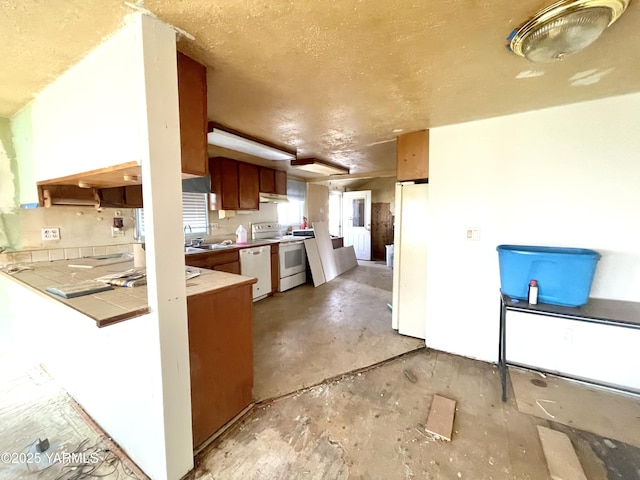 kitchen featuring concrete flooring, a sink, white appliances, tile countertops, and under cabinet range hood