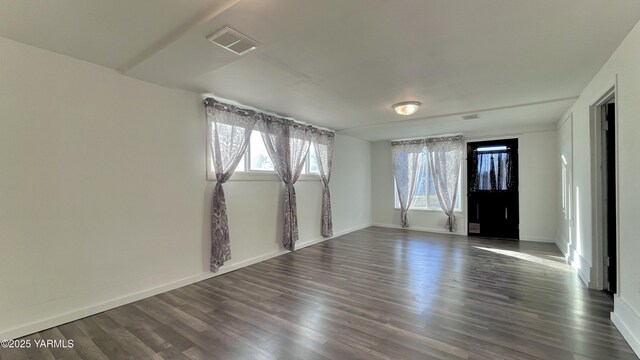 unfurnished room featuring visible vents, dark wood finished floors, and baseboards