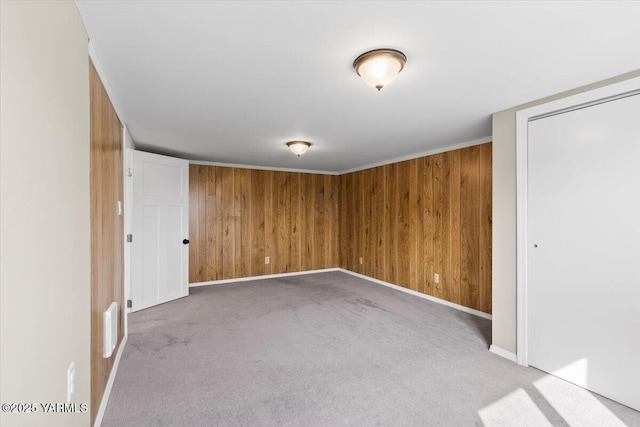 empty room featuring wooden walls, carpet floors, visible vents, and baseboards