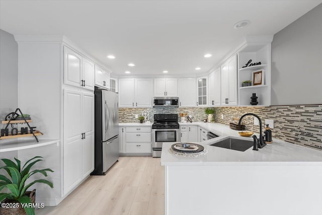 kitchen with stainless steel appliances, a peninsula, a sink, tasteful backsplash, and white cabinetry