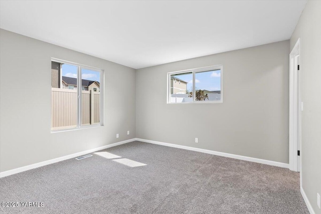 carpeted spare room with a wealth of natural light, visible vents, and baseboards