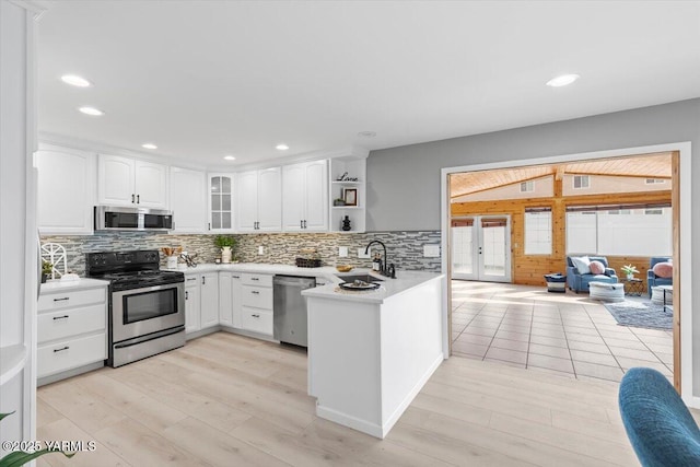 kitchen featuring white cabinets, a peninsula, a sink, light countertops, and appliances with stainless steel finishes