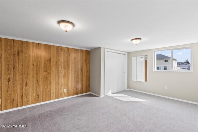 unfurnished bedroom featuring a closet, carpet flooring, wood walls, and baseboards