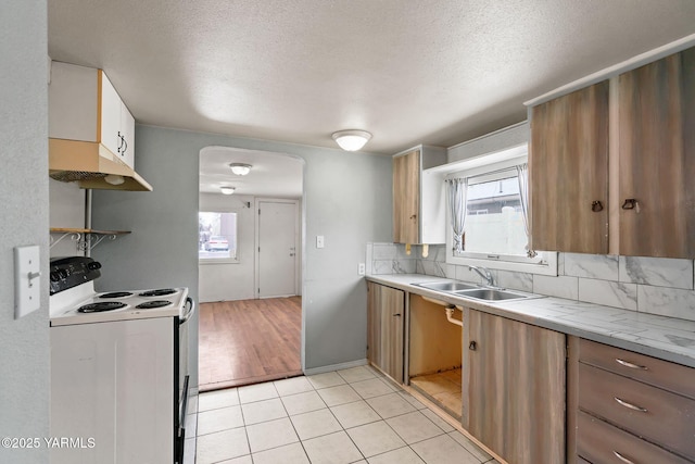 kitchen featuring white electric range oven, tasteful backsplash, light countertops, under cabinet range hood, and a sink