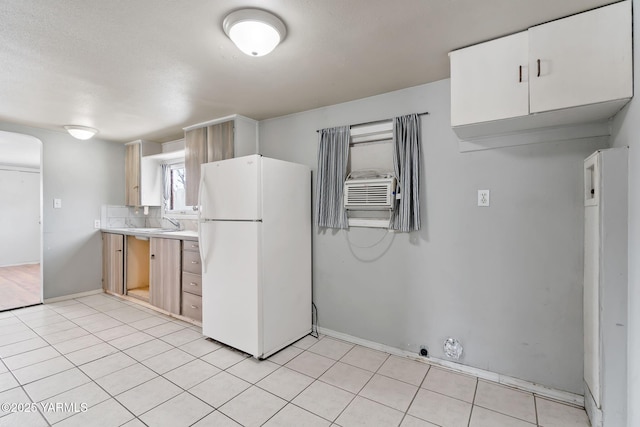 kitchen featuring arched walkways, light tile patterned floors, light countertops, backsplash, and freestanding refrigerator