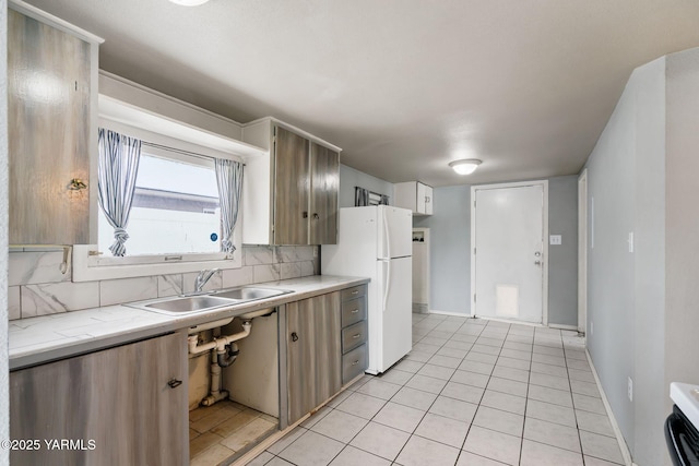 kitchen featuring light tile patterned floors, decorative backsplash, freestanding refrigerator, light countertops, and a sink