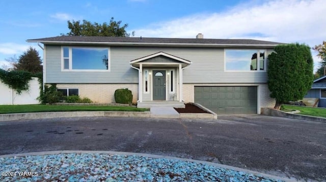 bi-level home featuring aphalt driveway, brick siding, a chimney, and a garage