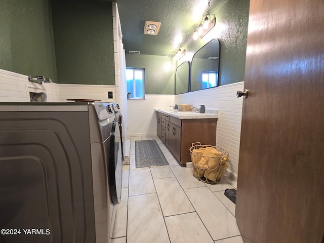 bathroom featuring a textured wall, a wainscoted wall, tile patterned flooring, vanity, and washing machine and dryer