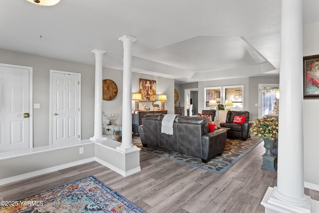 living area featuring wood finished floors, a raised ceiling, decorative columns, and baseboards