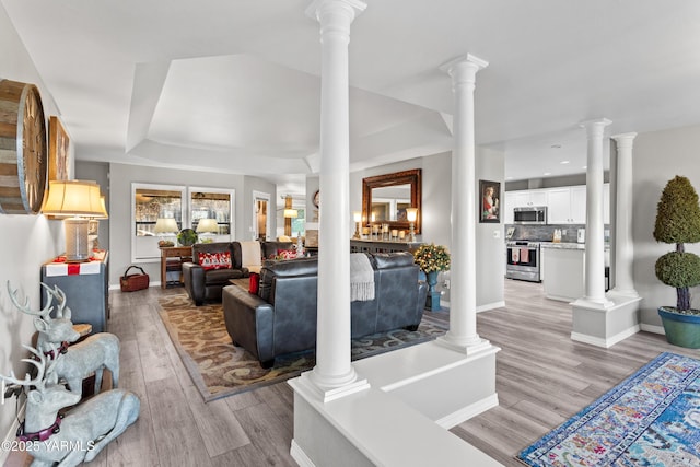 living room with decorative columns, baseboards, and light wood-style flooring