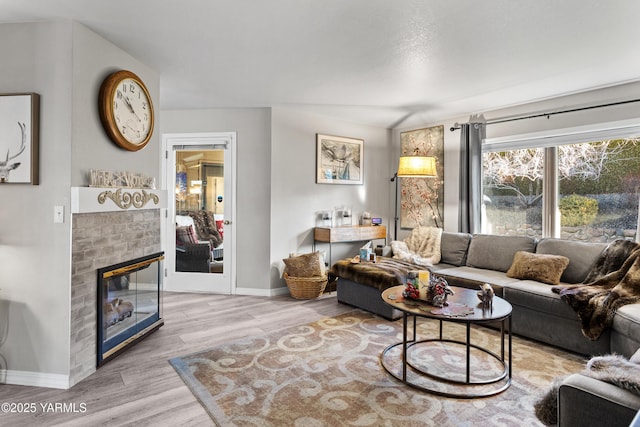 living area with a brick fireplace, light wood-style flooring, and baseboards