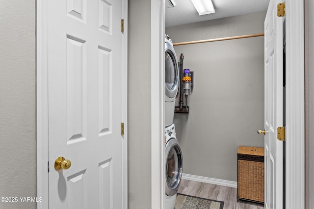 clothes washing area with laundry area, light wood finished floors, stacked washer / dryer, and baseboards