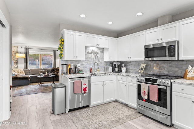 kitchen with appliances with stainless steel finishes, open floor plan, light stone countertops, white cabinetry, and a sink