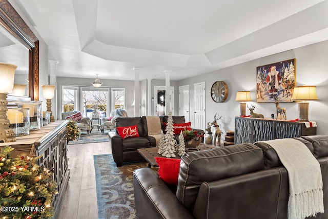 living area with a raised ceiling, ornate columns, and wood finished floors