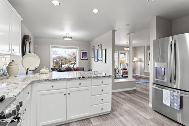 kitchen with decorative columns, stainless steel appliances, light wood-style flooring, white cabinetry, and light stone countertops