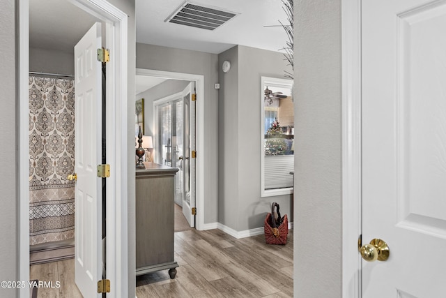 corridor with light wood-style flooring, visible vents, and baseboards