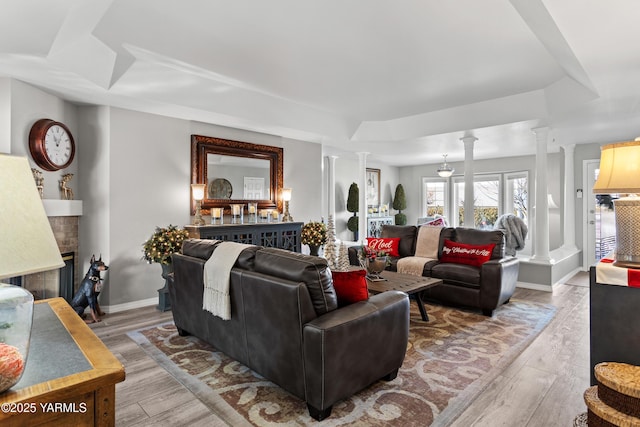 living room featuring ornate columns, baseboards, a fireplace with raised hearth, and wood finished floors