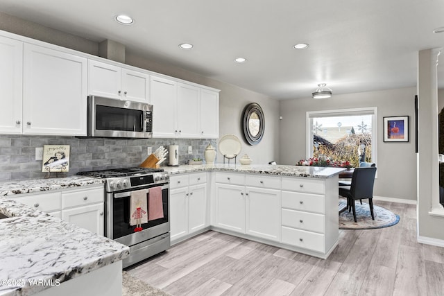 kitchen with tasteful backsplash, a peninsula, appliances with stainless steel finishes, and white cabinets