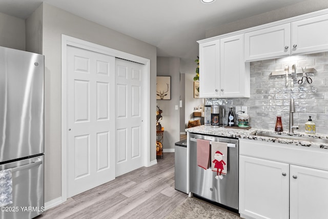 kitchen with stainless steel appliances, decorative backsplash, white cabinetry, a sink, and light wood-type flooring