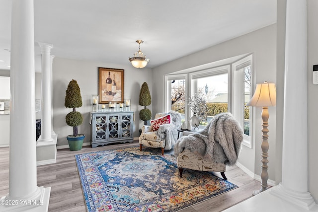 sitting room featuring ornate columns, baseboards, and light wood finished floors