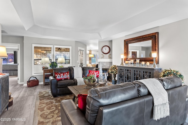 living area with a raised ceiling, visible vents, a glass covered fireplace, wood finished floors, and baseboards