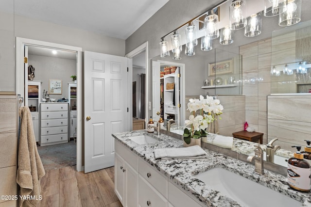 full bathroom featuring double vanity, a sink, a tile shower, and wood finished floors