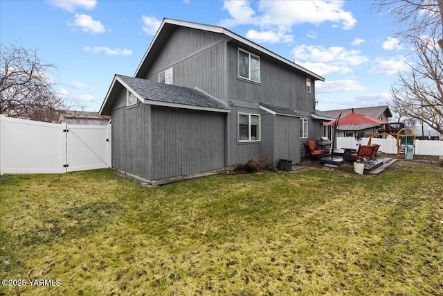 rear view of property featuring roof with shingles, fence, a yard, and a gate