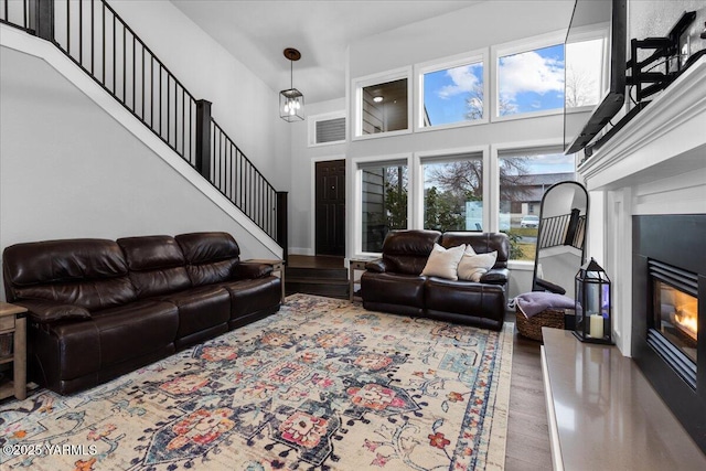 living area with stairs, a glass covered fireplace, a high ceiling, and wood finished floors