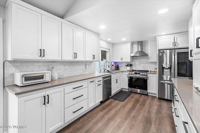 kitchen featuring a sink, dark wood finished floors, white cabinetry, stainless steel appliances, and wall chimney range hood